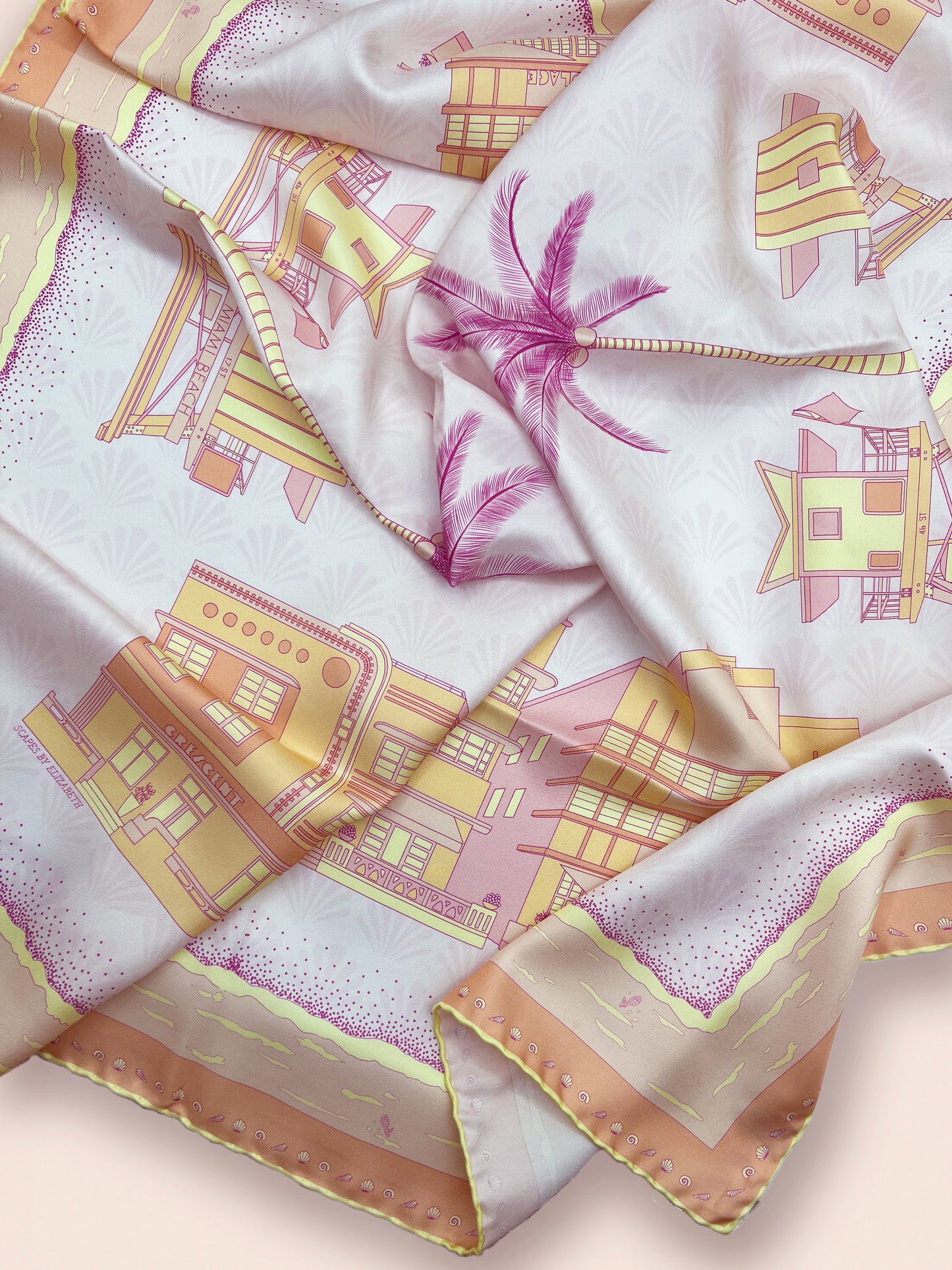 Close-up of the Sunset Miami Beach silk scarf showcasing hand-drawn miami beach Art Deco architecture, iconic miami beach lifeguard towers, palm trees, coastal scenery, and a subtle shell pattern in pink, yellow, and orange tones.