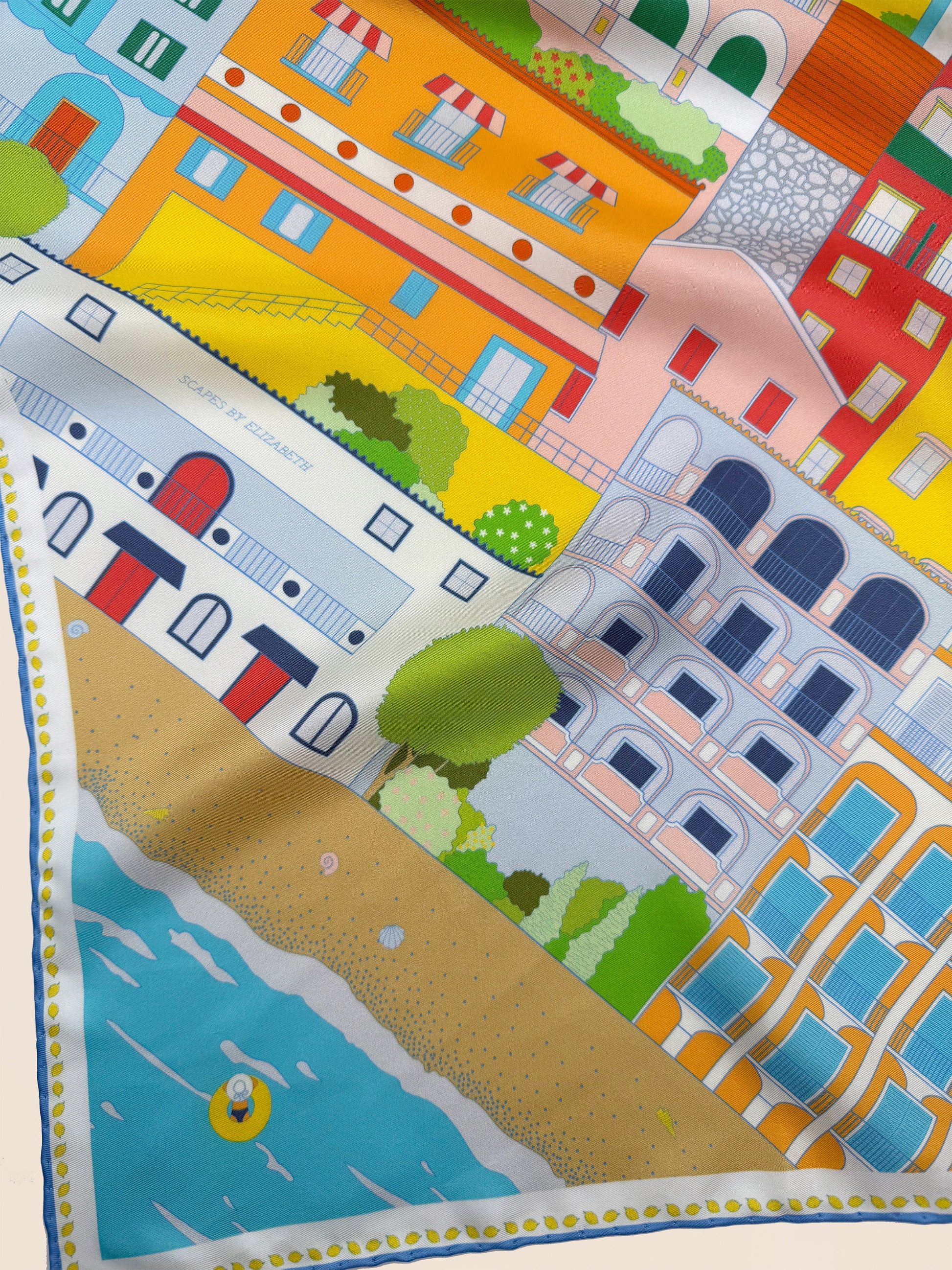 Close-up of the Amalfi Coast silk scarf in citrus splash showcasing hand-drawn Positano architecture, Mediterranean waters, colorful cliffside buildings, and coastal scenery inspired by Italy's Amalfi Coast.