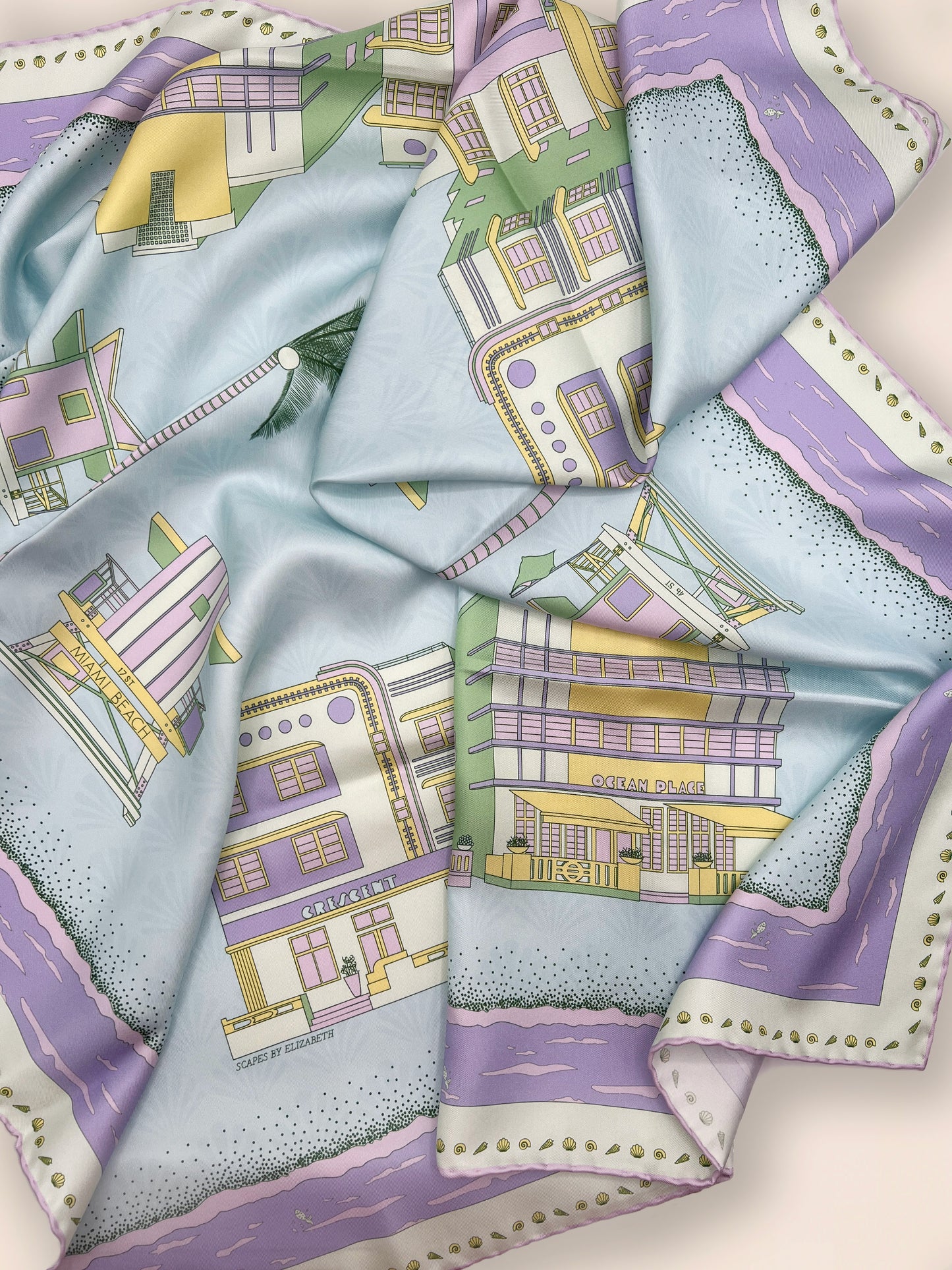 Close-up of the Pastel Miami Beach silk scarf showcasing hand-drawn iconic Miami beach Art Deco architecture, classic miami beach lifeguard towers, palm trees, coastal scenery, and a subtle shell pattern in pastel blue, green, purple, and yellow tones.