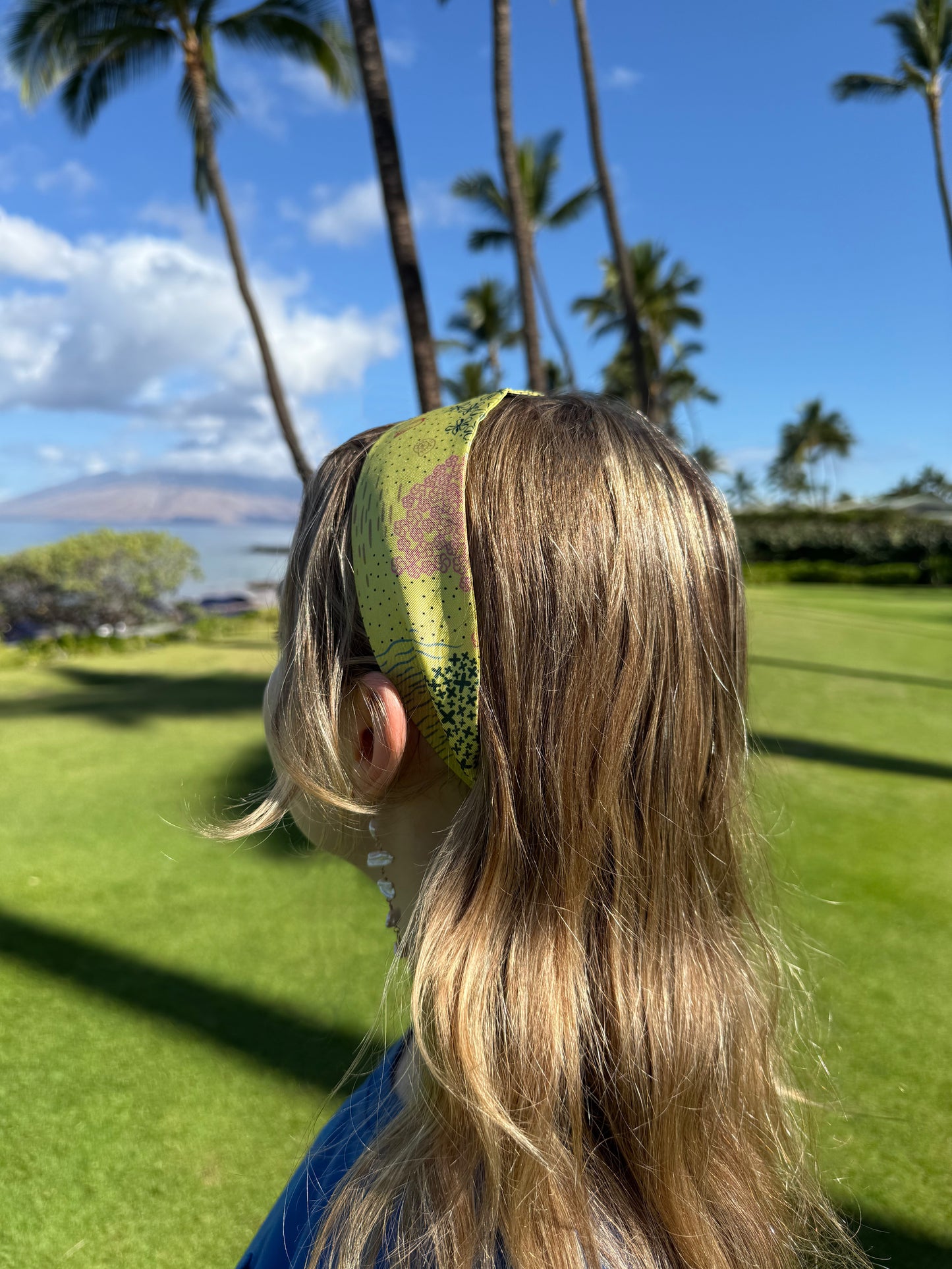 Woman wearing the Pineapple Yellow Hawaii silk twilly as a headband featuring colorful hand-drawn tropical flowers, coastal shells, ocean waves, and Hawaiian-inspired island motifs for a summer vacation outfit.