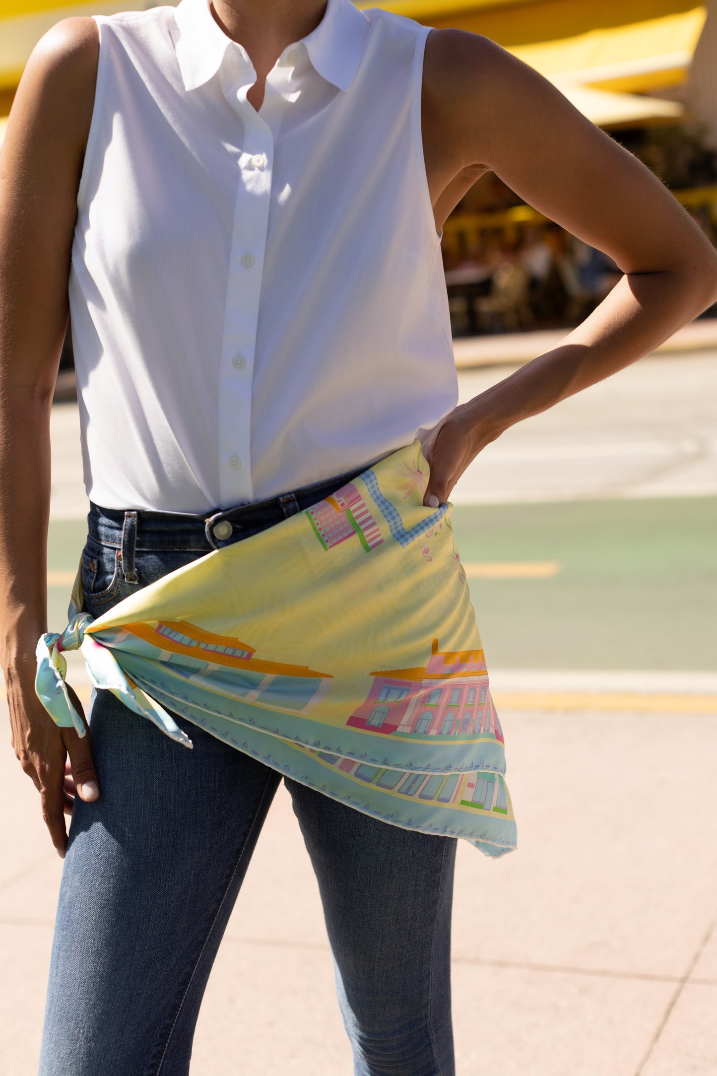 Woman styling the Pink Breeze Palm Beach silk scarf as a waist belt featuring hand-drawn Palm Beach architecture, iconic landmarks, palm trees, boats, and colorful Palm Beach-inspired artwork.