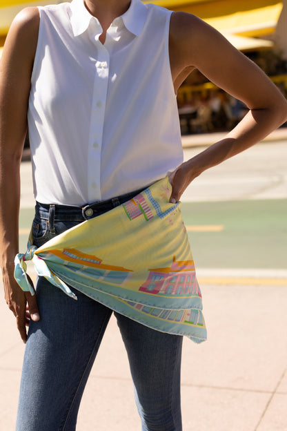 Woman styling the Pink Breeze Palm Beach silk scarf as a waist belt featuring hand-drawn Palm Beach architecture, iconic landmarks, palm trees, boats, and colorful Palm Beach-inspired artwork.