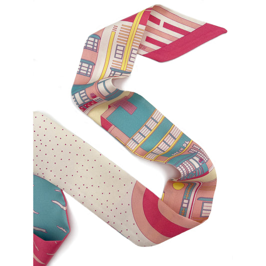 Rosy Splash Miami Beach silk twilly featuring hand-drawn Art Deco architecture, coastal scenery, and geometric design details in bright pink, turquoise, and yellow tones displayed in a folded lay-flat view showing both sides of the design.