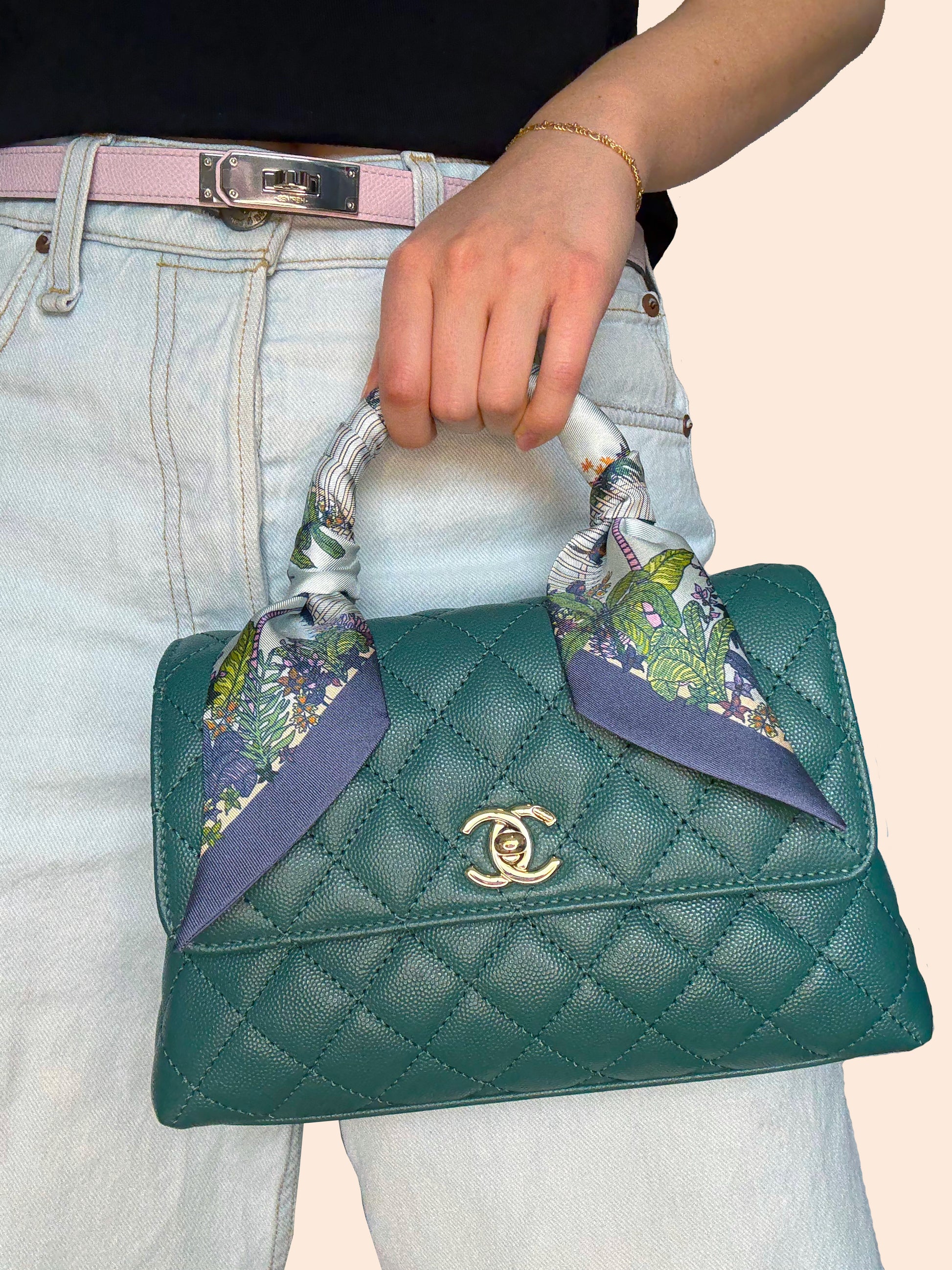 Seafoam Blue Key West silk twilly tied around the handle of a green handbag, featuring hand-drawn Key West-inspired landscape artwork in blue and green tones.