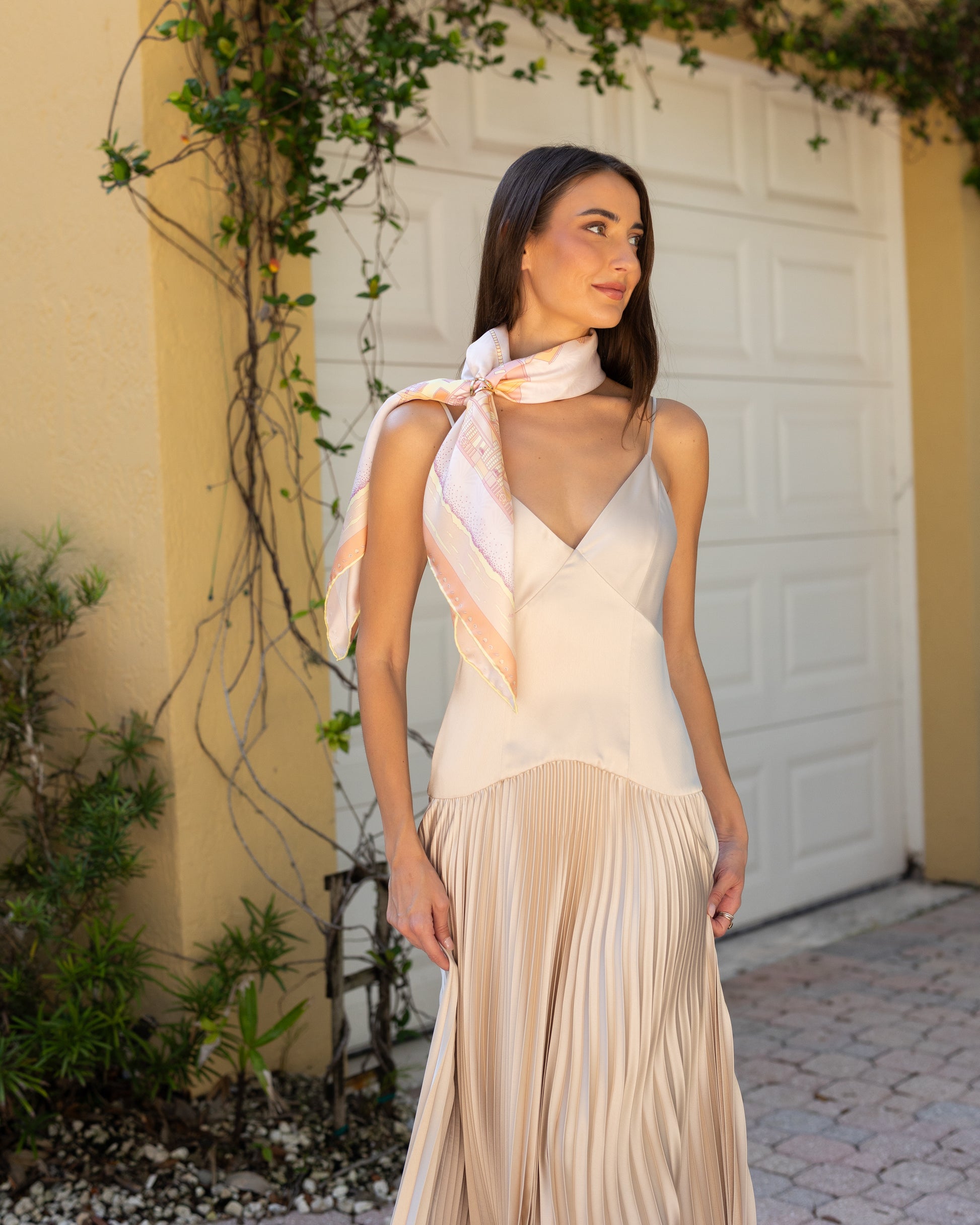 Woman wearing the Sunset Miami Beach silk scarf draped around her neck with a scarf ring and a gold evening dress, featuring hand-drawn miami Art Deco architecture, lifeguard towers, palm trees, and coastal-inspired artwork.