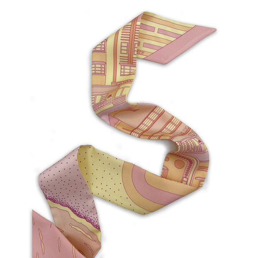Miami Beach silk twilly in Sunset colorway featuring hand-drawn Art Deco architecture and coastal scenery in pink, yellow, and orange tones inspired by a Miami sunset, displayed in a folded lay-flat view showing both sides of the design.